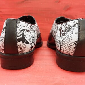 May include: A pair of black leather shoes with a white and black comic book print design. The shoes have a lace-up closure and a rounded toe.