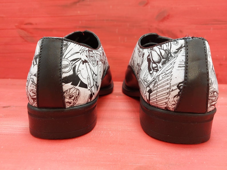 May include: A pair of black leather shoes with a white and black comic book print design. The shoes have a lace-up closure and a rounded toe.