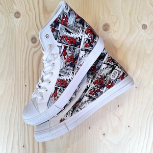 Può includere: Un paio di sneakers bianche alte con una stampa a fumetti con Spiderman. Le sneakers sono impilate l'una sull'altra.