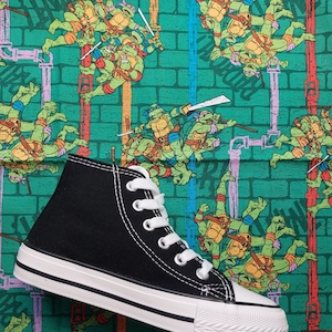 May include: Black high-top canvas sneakers with white laces and a white rubber sole. The sneakers are on a green background with a repeating pattern of Teenage Mutant Ninja Turtles.