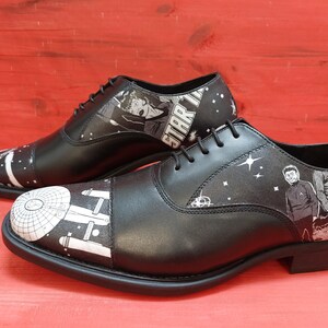 May include: A pair of black leather Oxford shoes with a white and black Star Trek themed design. The shoes feature images of the Star Trek crew and the Enterprise spaceship.