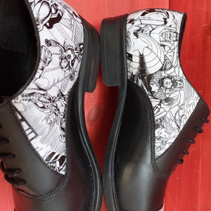 May include: A pair of black leather lace-up shoes with a white and black comic book print featuring superheroes.