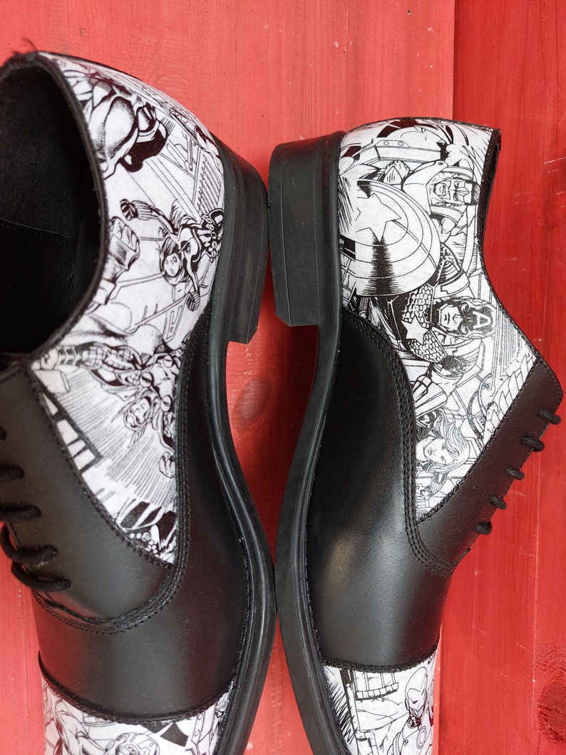 May include: A pair of black leather lace-up shoes with a white and black comic book print featuring superheroes.