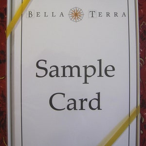 May include: A white card with black text that reads "Bella Terra" with a compass symbol in between the words. The text "Sample Card" is printed below the logo.