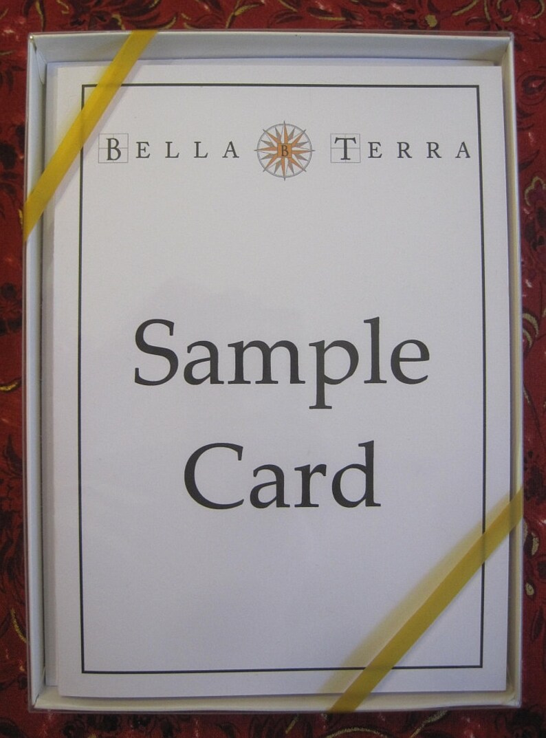 May include: A white card with black text that reads "Bella Terra" with a compass symbol in between the words. The text "Sample Card" is printed below the logo.