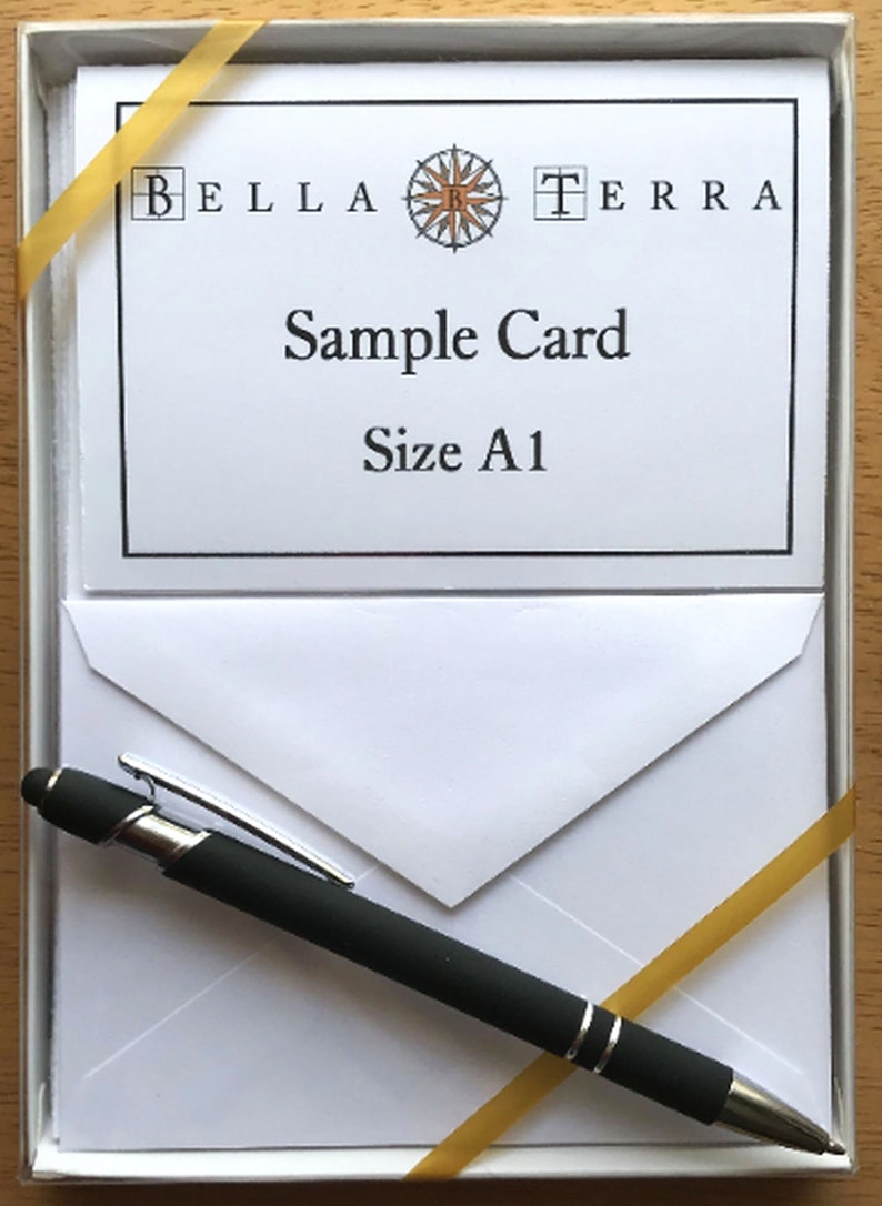 May include: A white card with a black border and the text "Bella Terra" with a compass logo in the center. The text "Sample Card" and "Size A1" are below the logo. The card is in a white box with a gold ribbon and a black pen.
