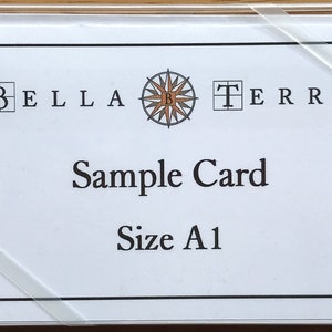 May include: A white card with black text that reads "Bella Terra" with a compass logo in the center and "Sample Card" and "Size A1" below the logo.