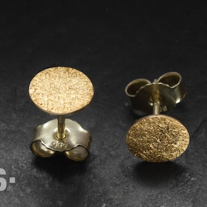May include: A pair of gold-toned stud earrings with a textured circular design. The earrings are made of metal and have a post-back closure.
