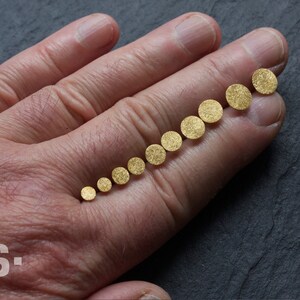 May include: A set of ten gold-colored round discs of varying sizes, arranged in order from smallest to largest on a person's hand.