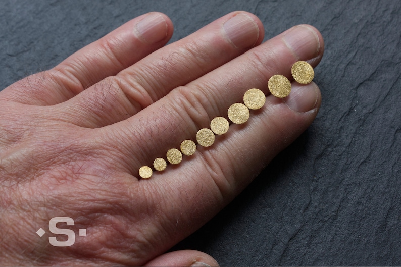 May include: A set of ten gold-colored round discs of varying sizes, arranged in order from smallest to largest on a person's hand.