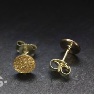 May include: A pair of gold stud earrings with a textured round design. The earrings have a post and butterfly back.