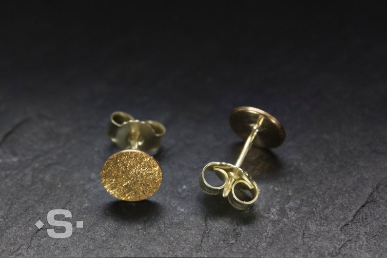 May include: A pair of gold stud earrings with a textured round design. The earrings have a post and butterfly back.