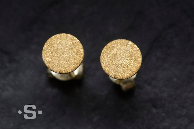 May include: A pair of gold-toned stud earrings with a textured circular design.