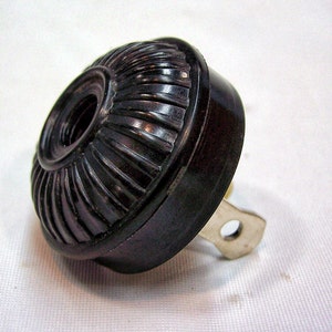 May include: A black plastic electrical outlet adapter with a ribbed design and a metal prong.