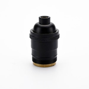 May include: A black lamp socket with a textured, cylindrical body and a rounded top. The socket has a brass-colored base and is designed to hold a light bulb. The overall design is simple and functional.