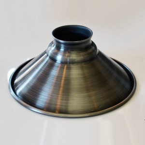 May include: A silver metal lampshade with a wide, flared opening and a narrow base. The shade has a brushed finish and a slightly distressed look.