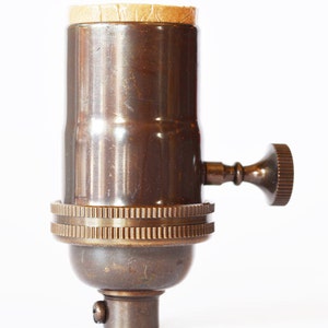 May include: A brass light bulb socket with a side switch. The socket has a threaded base and a paper-covered top.