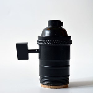 May include: A black metal light bulb socket with a side switch. The socket has a threaded base and a textured finish.