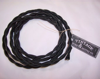 May include: Black electrical cord with a braided fabric covering. The cord is coiled and tied with twine. A black and white label with the text "Vintage Wire & Supply Co." is attached to the cord.