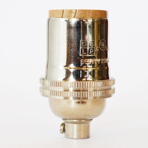 May include: A chrome light bulb socket with a brown paper insulator on the top. The socket has a UL listing and the text "66W 72506" is visible.