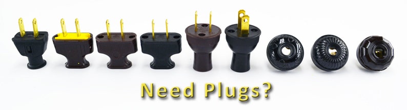 Puede incluir: Surtido de enchufes el&eacute;ctricos en varios estilos y colores, incluyendo negro, marr&oacute;n y amarillo. Los enchufes est&aacute;n dispuestos en una fila sobre una superficie blanca. El texto "Need Plugs?" est&aacute; escrito en amarillo debajo de los enchufes.