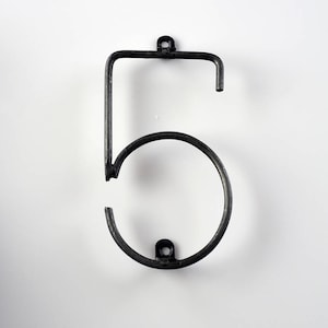 May include: A black metal house number five. The number is made of a single piece of metal that is bent into the shape of a five. The number has two small holes at the top and bottom for hanging.