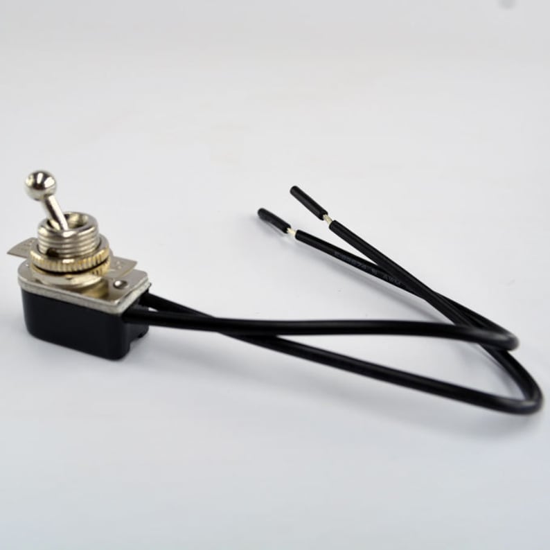 Puede incluir: Un interruptor de palanca negro y plateado con una perilla redonda y dos cables negros. El interruptor est&aacute; montado en una base de pl&aacute;stico negro.