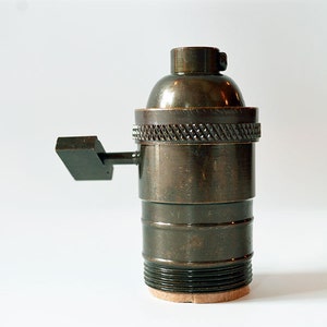 May include: A bronze-colored electrical socket with a side switch. The socket has a threaded base and a decorative knurled ring.