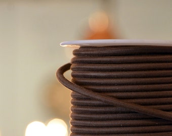 May include: A spool of brown fabric cord, wound tightly on a white plastic spool.