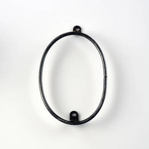 May include: Black metal oval frame with two small hooks on the top and bottom.