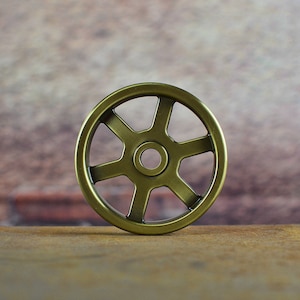 May include: A gold-coloured metal wheel with six spokes and a central hole. The wheel is sitting on a wooden surface.