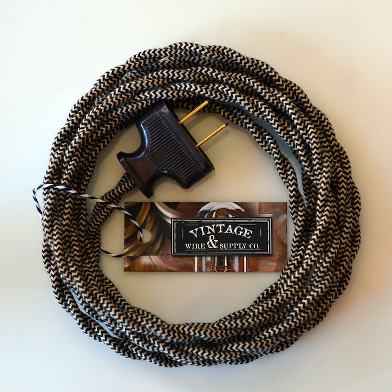 May include: A coiled electrical cord with a black and cream chevron pattern. A dark brown plug is attached. A tag with the text "VINTAGE WIRE & SUPPLY CO." is included.