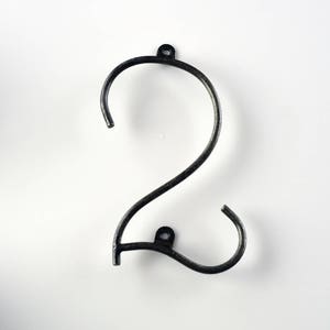 May include: Black metal house number two. The number is made of a single piece of metal that is bent into the shape of a two. The number is attached to a wall with two screws.