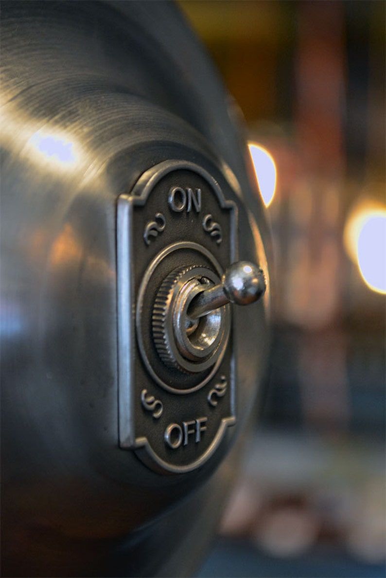 Puede incluir: Un interruptor de luz de metal plateado con un interruptor de palanca y una perilla redonda. El interruptor est&aacute; etiquetado como "ON" y "OFF".