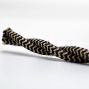 May include: Close-up of a length of rope with a black and tan chevron pattern. The rope is tightly woven and has a slightly fuzzy texture. The background is plain white.
