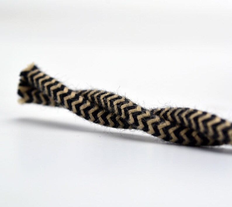 May include: Close-up of a length of rope with a black and tan chevron pattern. The rope is tightly woven and has a slightly fuzzy texture. The background is plain white.