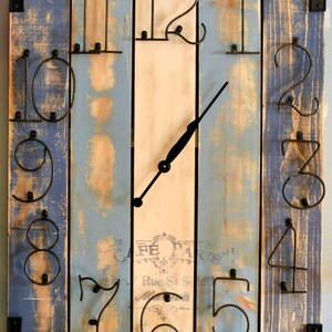 Puede incluir: Un reloj de madera r&uacute;stico con n&uacute;meros de metal. La esfera del reloj est&aacute; pintada de blanco con un aspecto desgastado y tiene una aguja de reloj de metal negro. Los n&uacute;meros est&aacute;n fijados a la madera con clavos. El reloj est&aacute; hecho de madera recuperada y tiene un aspecto desgastado. El reloj es una forma &uacute;nica y elegante de a&ntilde;adir un toque de encanto r&uacute;stico a cualquier hogar.