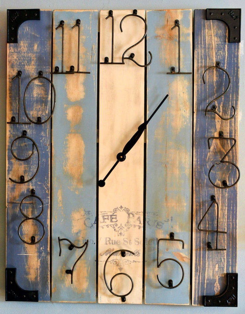 Puede incluir: Un reloj de madera r&uacute;stico con n&uacute;meros de metal. La esfera del reloj est&aacute; pintada de blanco con un aspecto desgastado y tiene una aguja de reloj de metal negro. Los n&uacute;meros est&aacute;n fijados a la madera con clavos. El reloj est&aacute; hecho de madera recuperada y tiene un aspecto desgastado. El reloj es una forma &uacute;nica y elegante de a&ntilde;adir un toque de encanto r&uacute;stico a cualquier hogar.