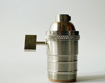 May include: A silver metal light bulb socket with a side switch. The socket has a threaded base and a decorative ring around the top.