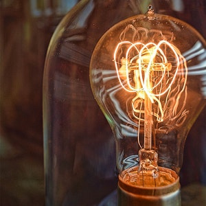 May include: A vintage-style light bulb with a coiled filament glows brightly inside a clear glass dome.