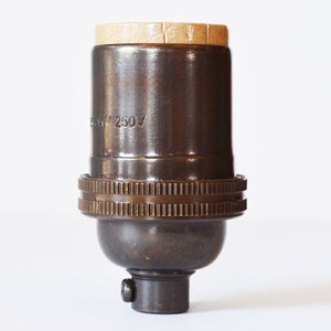 May include: A brown ceramic light bulb socket with a brass threaded base and a cardboard insulator. The socket is labeled "250V".