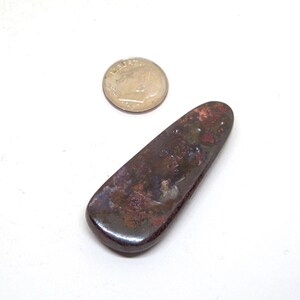 May include: A dark brown, iridescent, teardrop-shaped opal cabochon with a smooth, polished surface. The opal is approximately the size of a U.S. dime.