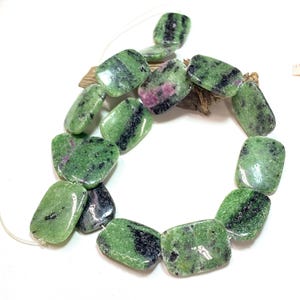 May include: A strand of rectangular zoisite beads. The beads are a mix of green, black, and pink. The beads are strung on a thin, clear cord. The beads are smooth and polished.