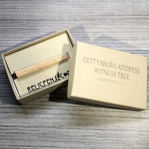 May include: A wooden tie bar with a black metal clasp in a brown cardboard box. The box has the text "Gettysburg Address Witness Tree" and "Handcrafted in the USA by RelicPens.com".
