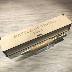 May include: A wooden pen with a brass tip and a metal clip. The pen is engraved with the words "Battle of Tinian 1944". The pen is in a wooden box with the same inscription.