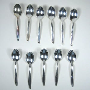 Puede incluir: Un juego de doce cucharas brillantes de color plateado, dispuestas en dos filas de seis. Cada cuchara tiene un cuenco redondeado y un mango largo y delgado. Las cucharas son reflectantes.