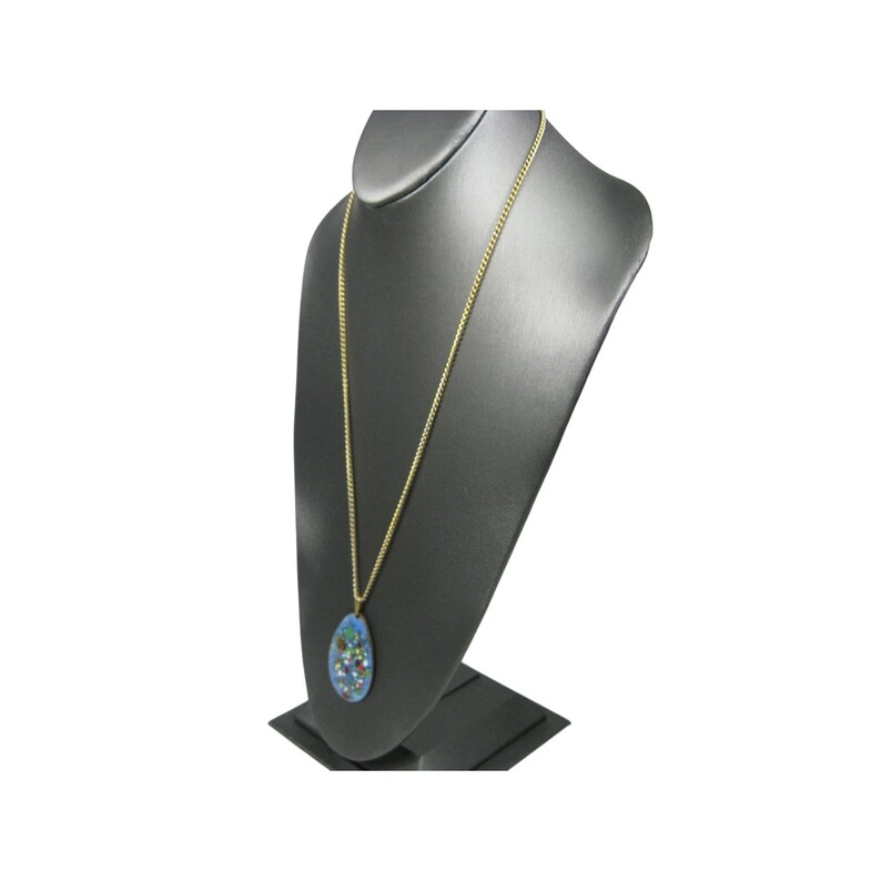 Puede incluir: Un collar de cadena dorada con un colgante en forma de l&aacute;grima. El colgante tiene un fondo azul con dise&ntilde;os florales y abstractos coloridos. El collar se exhibe en un busto de joyer&iacute;a negro.