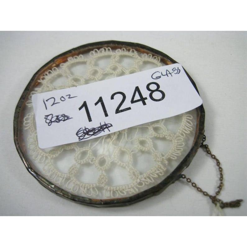 Pu&ograve; includere: Un ciondolo rotondo in vetro in stile antico con un inserto in pizzo color crema. Il ciondolo ha una montatura in metallo e una piccola catena. Un'etichetta bianca con il numero "11248" &egrave; attaccata al ciondolo.