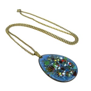 Puede incluir: Un collar de cadena dorada con un colgante. El colgante tiene forma ovalada con un fondo de esmalte azul claro y un dise&ntilde;o moteado colorido. El collar es de estilo vintage.