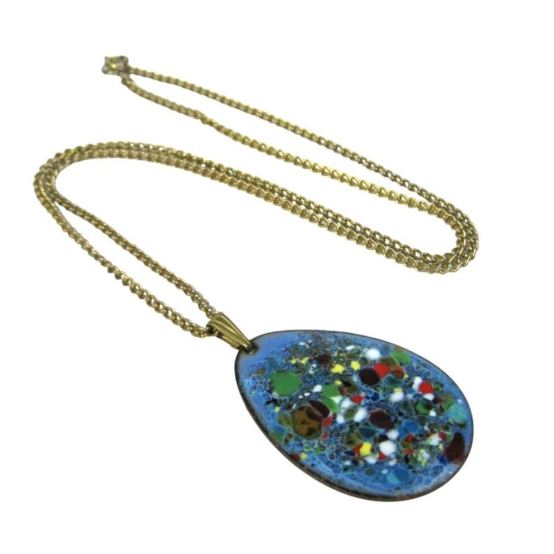 Puede incluir: Un collar de cadena dorada con un colgante. El colgante tiene forma ovalada con un fondo de esmalte azul claro y un dise&ntilde;o moteado colorido. El collar es de estilo vintage.